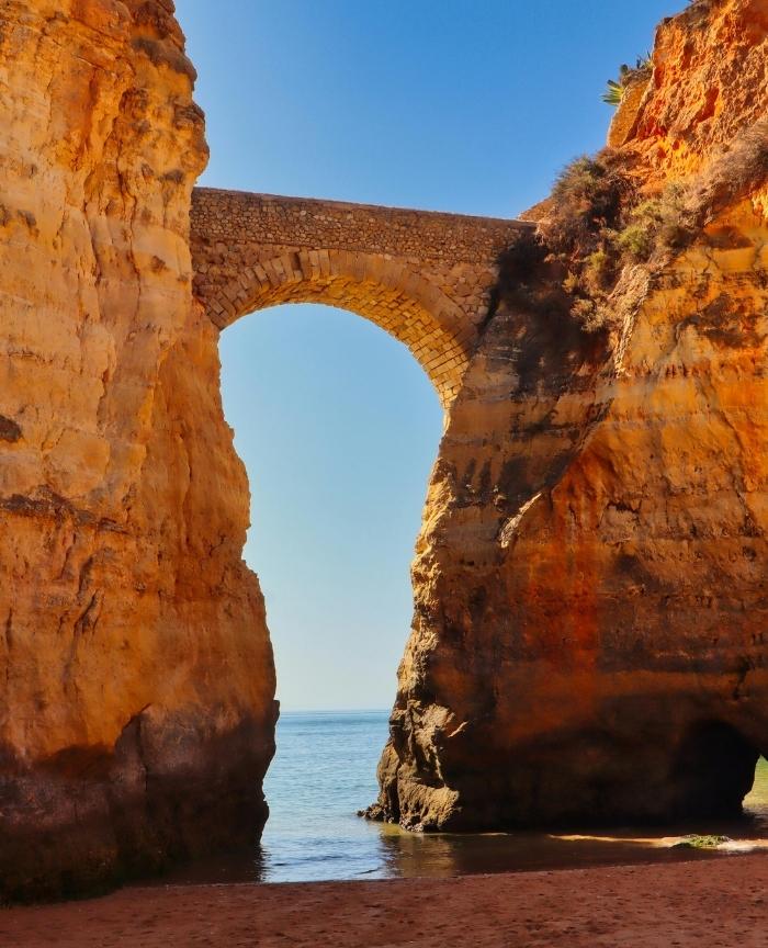 English: The iconic stone arch bridge at Praia dos Estudantes connecting two towering cliffs over the beach in Lagos Portugal Português: A icónica ponte de pedra na Praia dos Estudantes a ligar duas falésias sobre a praia em Lagos, Portugal