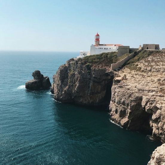 A panoramic view of the Cabo de São Vicente lighthouse on a rugged cliff overlooking the vast blue Atlantic Ocean. Uma vista panorâmica do farol do Cabo de São Vicente no topo de uma falésia sobre o vasto oceano Atlântico