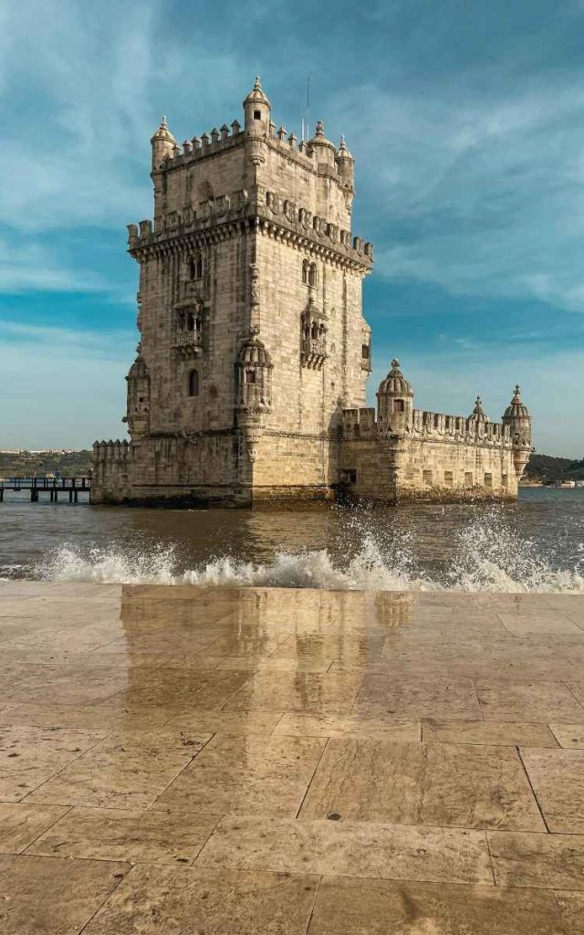English: The historic Belém Tower with a wave splashing onto the stone promenade in Lisbon Portugal Português: A histórica Torre de Belém com uma onda a rebentar no passeio de pedra em Lisboa, Portugal
