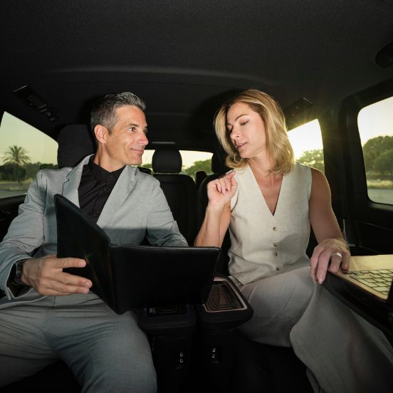 English: Two business professionals working on a laptop in the spacious back seat of a luxury car during a corporate transfer Português: Dois profissionais a trabalhar num portátil no assento traseiro de um carro de luxo durante um transfer executivo