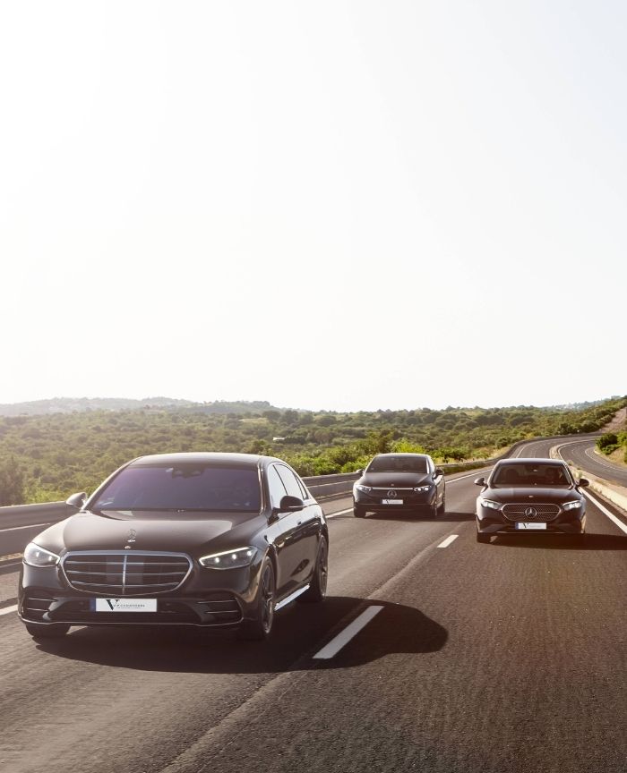 English: A line of black Mercedes-Benz luxury sedans driving on a sunny road in the Algarve Portugal Português: Uma fila de sedans de luxo pretos da Mercedes-Benz a circular numa estrada ensolarada no Algarve