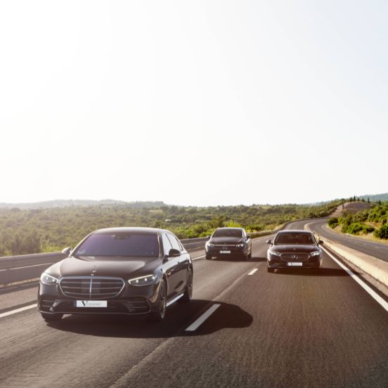 English: A line of black Mercedes-Benz luxury sedans driving on a sunny road in the Algarve Portugal Português: Uma fila de sedans de luxo pretos da Mercedes-Benz a circular numa estrada ensolarada no Algarve