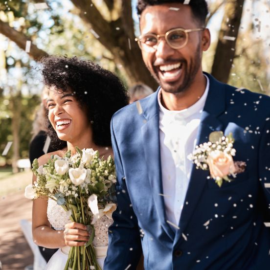 English: A happy bride and groom laughing and celebrating on their wedding day as confetti falls around them Português: Uma noiva e um noivo felizes a rir e a celebrar o seu dia de casamento com confetes a cair à sua volta